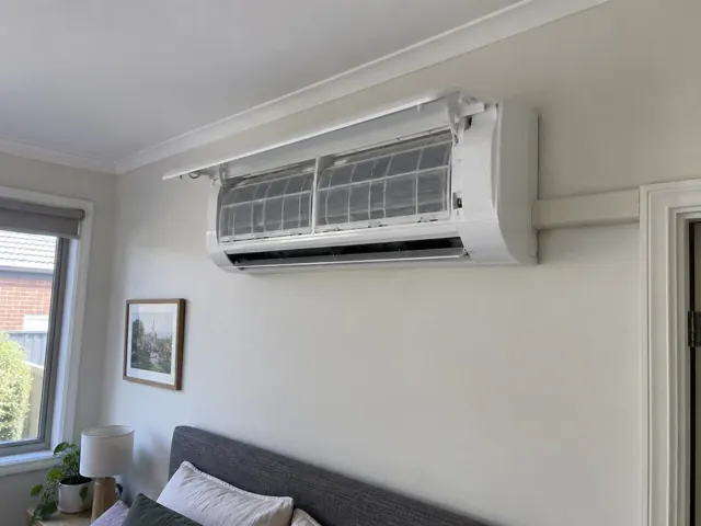 Clean split-system head on a pale wall in a living room with open front panel and visible filters in Mile End
