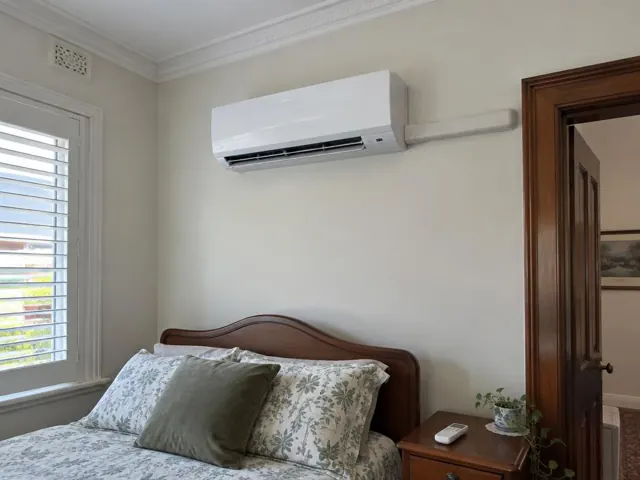 Clean split system mounted high on a bedroom wall above a bed, with pipe cover and louvre open in Adelaide